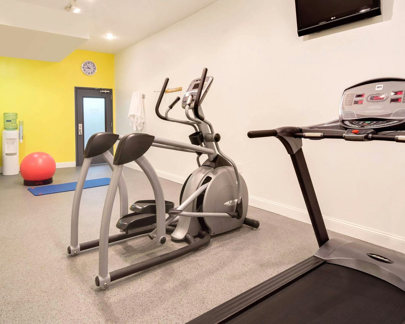 Hotel fitness room with elliptical, treadmill, and yoga equipment.