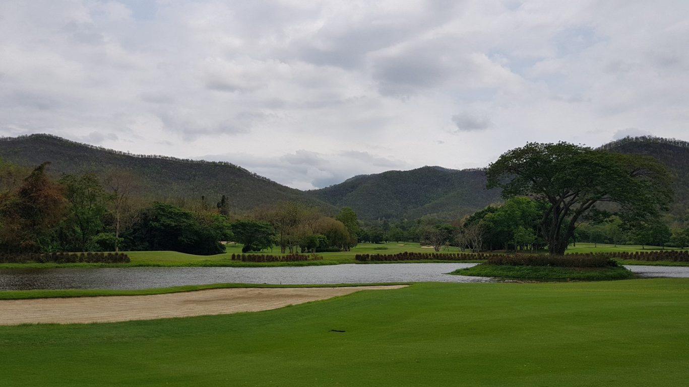 Lush green golf course with mountains and water feature.