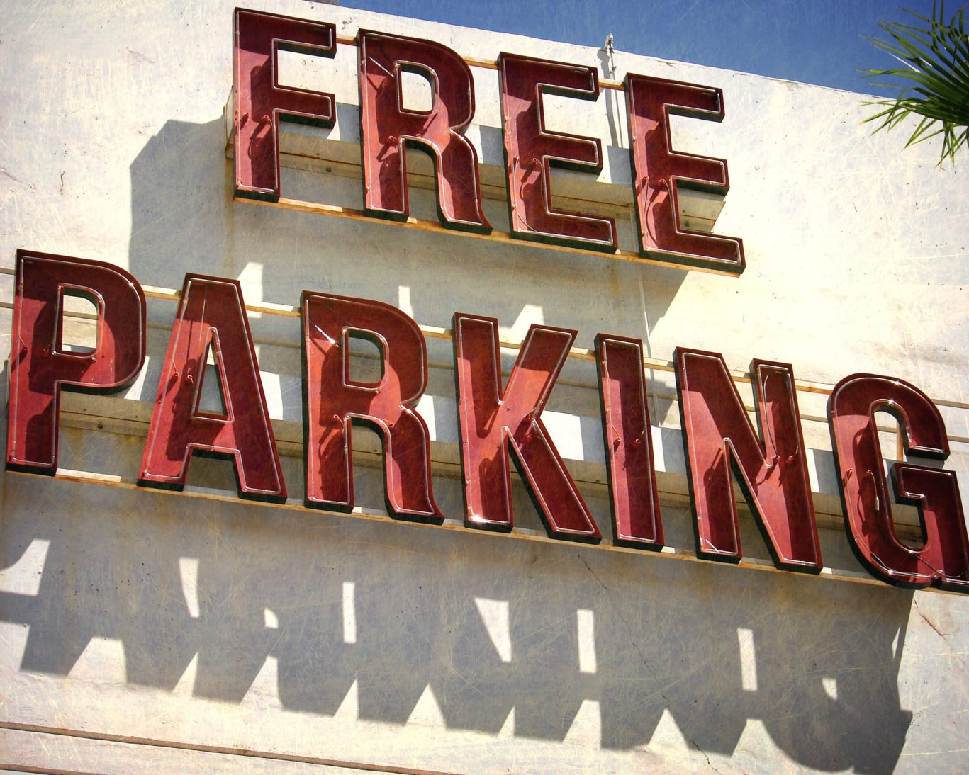 Vintage red neon sign advertising free parking against a sunny backdrop.