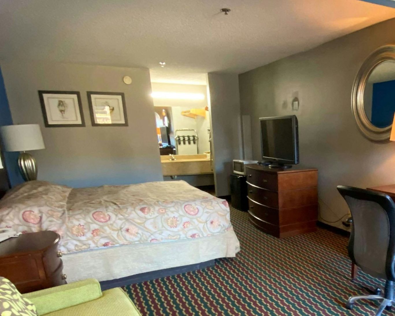 Cozy hotel room with king bed, TV, desk, and vanity area.