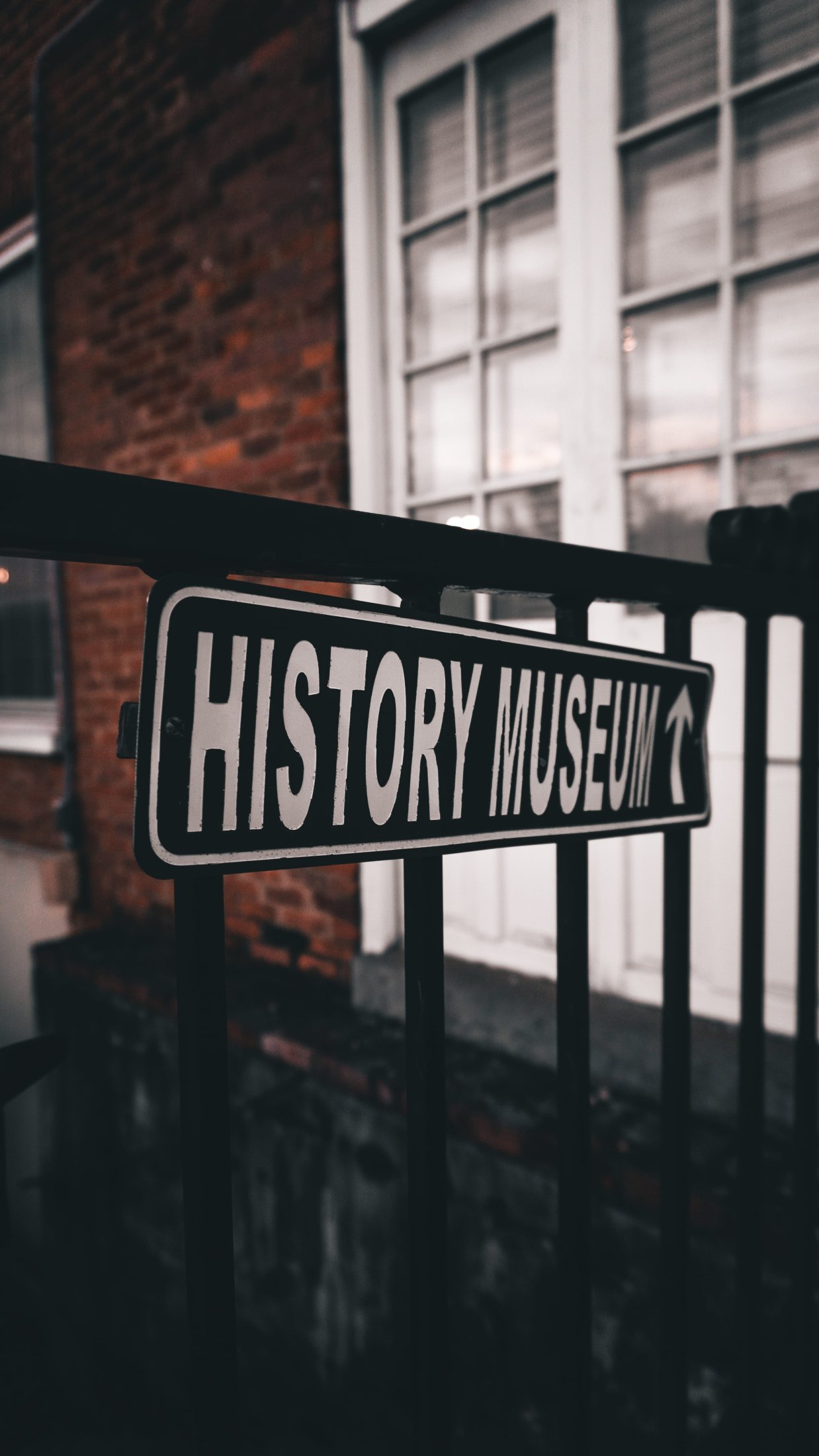 Close-up of vintage-style ‘History Museum’ directional sign on iron railing.