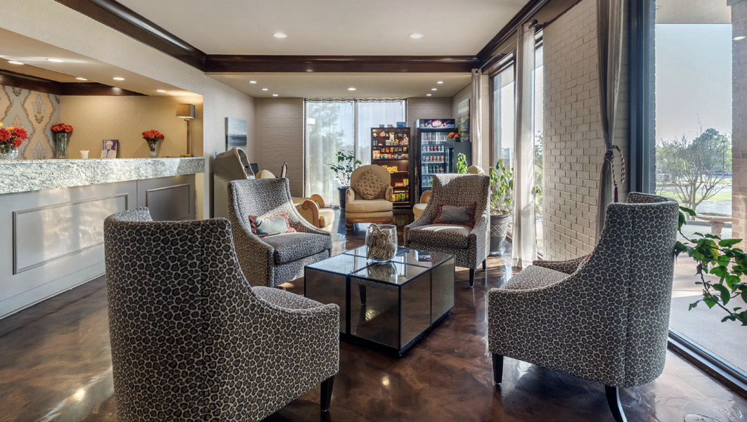 Modern hotel lobby with patterned armchairs, reception desk, and large windows letting in natural light.