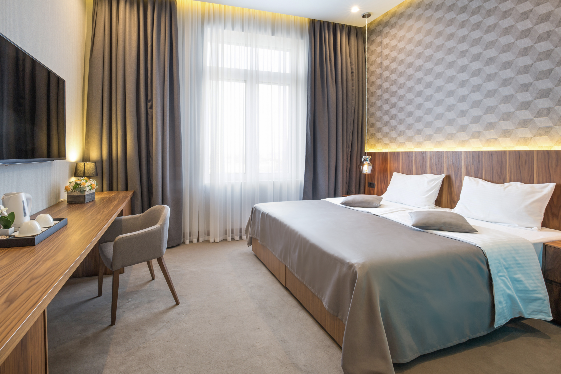 Modern hotel room with a large bed, wood accents, and a cozy work desk.