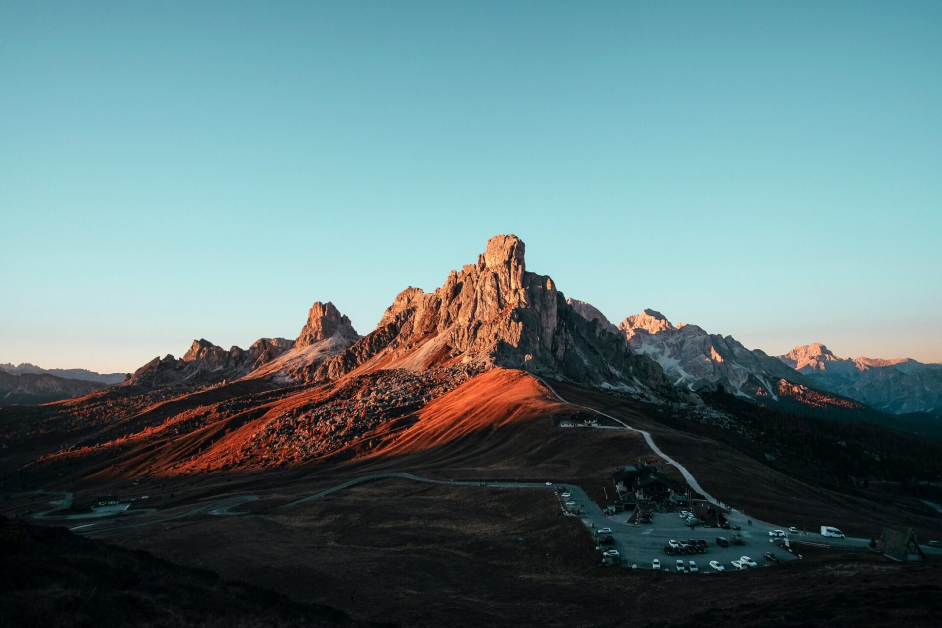 Majestic mountain peaks illuminated by sunset light, overlooking a winding road and a small settlement below.