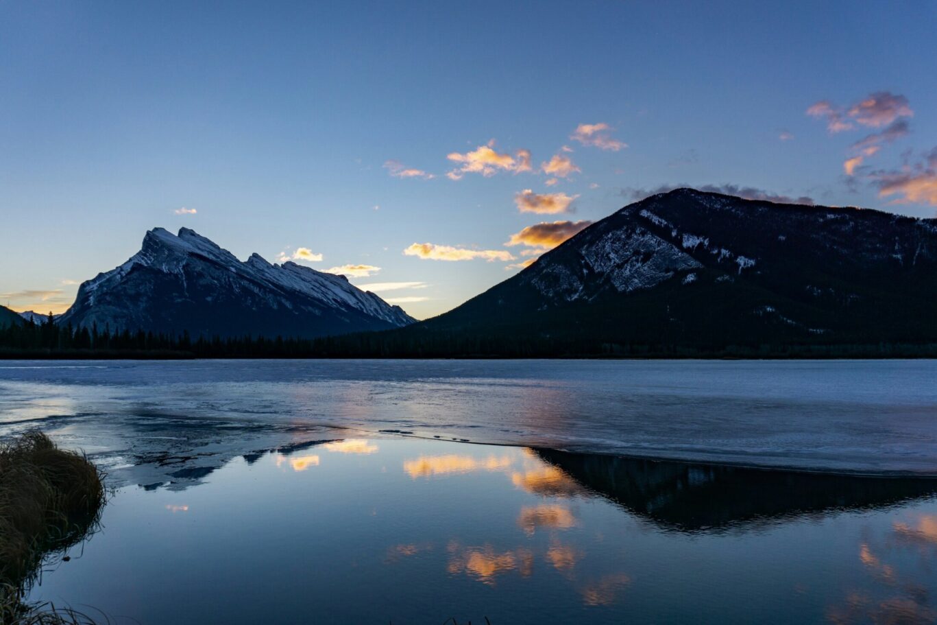 Snow-capped mountains reflected on a calm lake during sunset with a colorful sky.