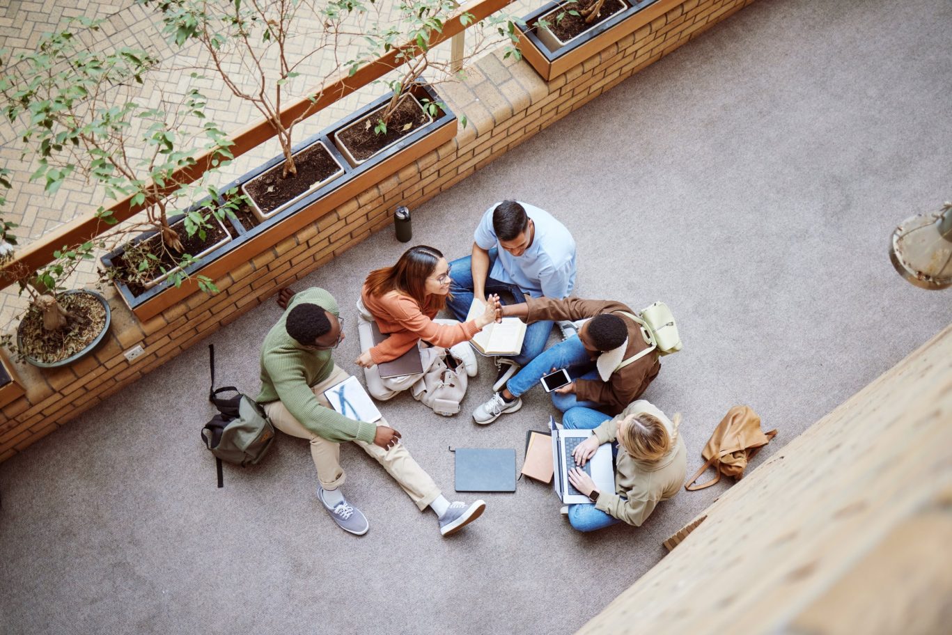 Top view of diverse university students sitting on the floor, collaborating and celebrating with a high five during a group study session.