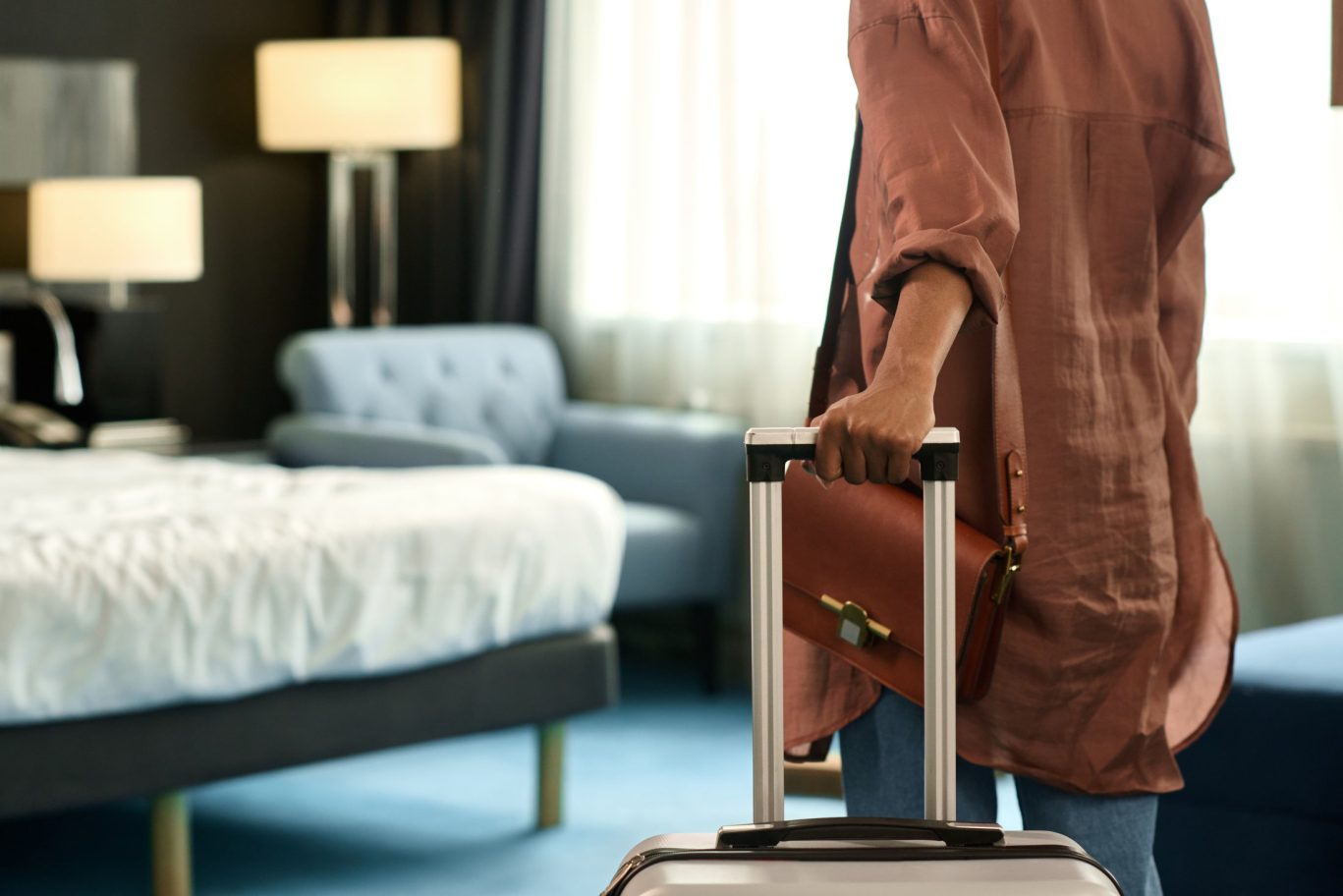 Close-up of a Black woman walking away from the picture and entering a hotel room with a suitcase, ready for her stay.